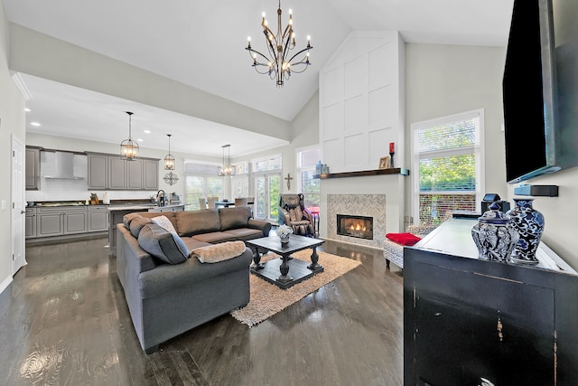 living area with high vaulted ceiling, dark wood-style floors, a chandelier, healthy amount of natural light, and a tiled fireplace