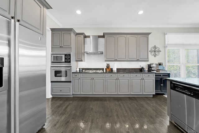 kitchen with appliances with stainless steel finishes, wall chimney exhaust hood, gray cabinetry, crown molding, and tasteful backsplash