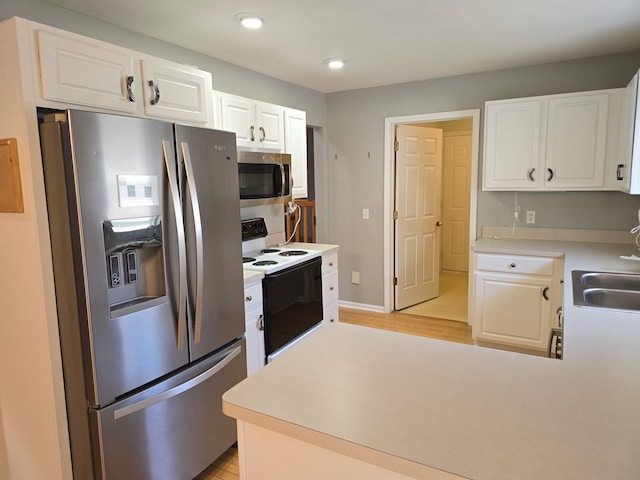 kitchen with appliances with stainless steel finishes, light wood finished floors, white cabinetry, light countertops, and a peninsula