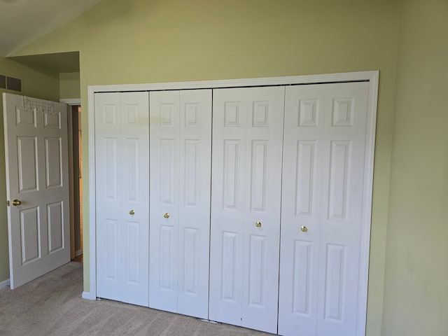 unfurnished bedroom with light colored carpet, a closet, lofted ceiling, and baseboards