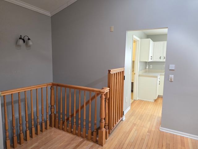 hall featuring an upstairs landing, light wood-type flooring, crown molding, and baseboards