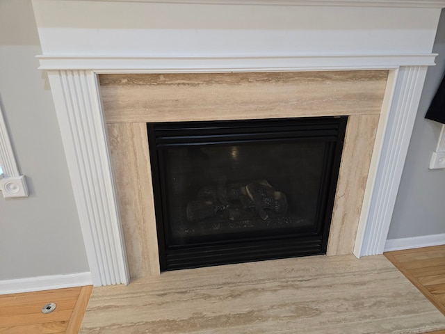 detailed view of a fireplace, wood finished floors, and baseboards