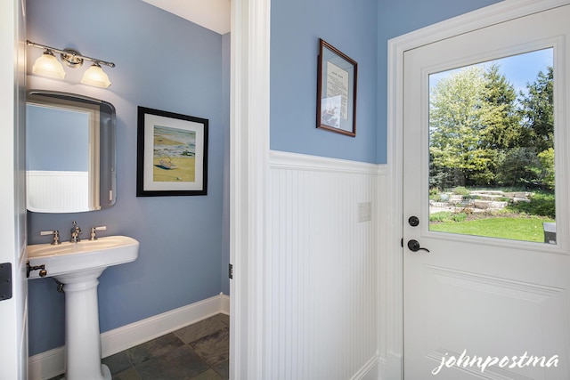 bathroom featuring stone finish floors, baseboards, a sink, and a wainscoted wall