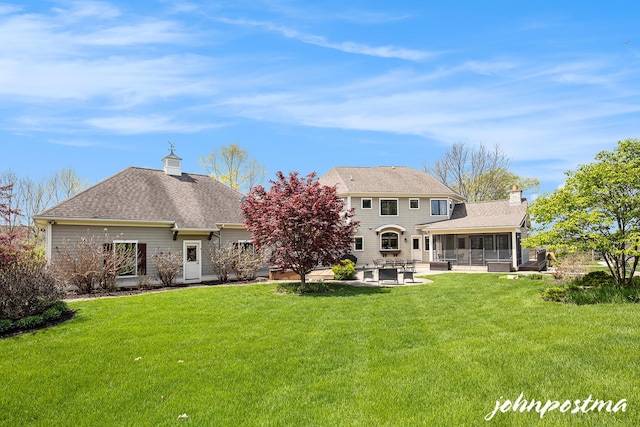 rear view of property featuring a sunroom, a patio area, a chimney, and a lawn