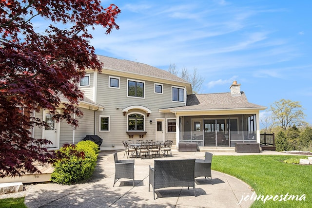 rear view of house with a sunroom, a patio, a chimney, a lawn, and roof with shingles