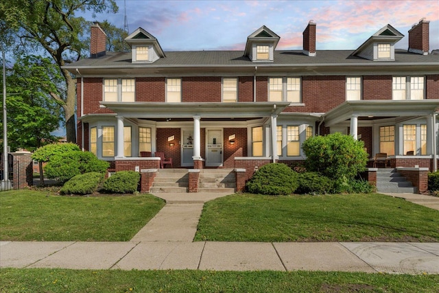 american foursquare style home with a porch, a yard, brick siding, and a chimney