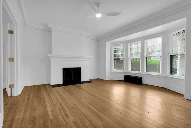 unfurnished living room featuring ceiling fan, light wood finished floors, crown molding, a brick fireplace, and baseboards