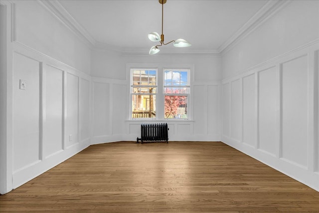 unfurnished dining area featuring a decorative wall, radiator heating unit, a chandelier, crown molding, and wood finished floors