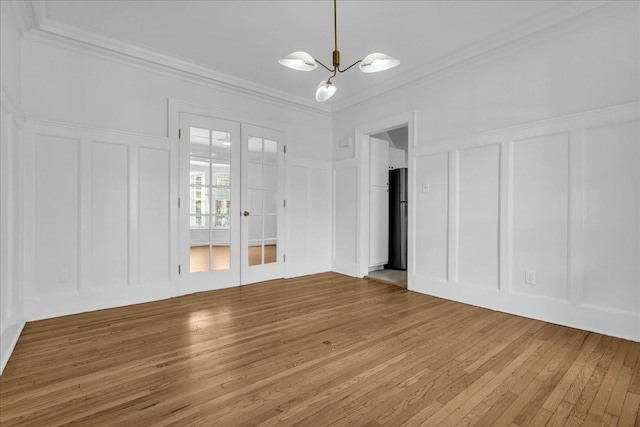 unfurnished living room featuring a decorative wall, hardwood / wood-style flooring, a chandelier, crown molding, and french doors