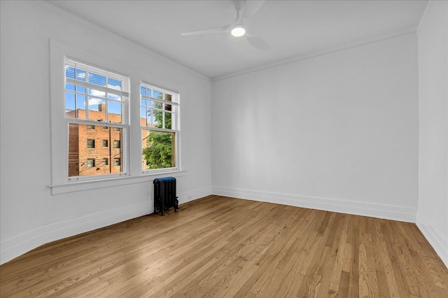 spare room featuring radiator heating unit, light wood-style flooring, ornamental molding, baseboards, and a ceiling fan