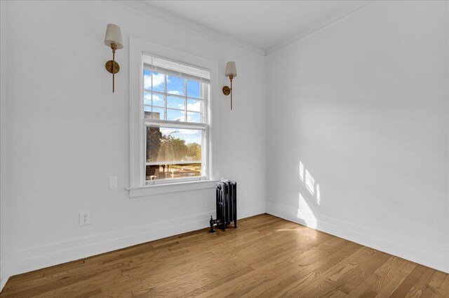 spare room with radiator heating unit, ornamental molding, wood finished floors, and baseboards