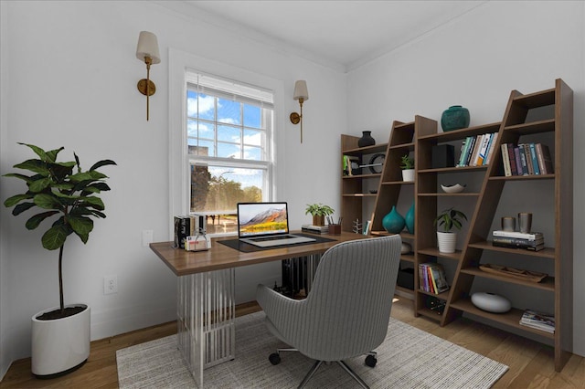 office area featuring wood finished floors, ornamental molding, built in desk, and baseboards