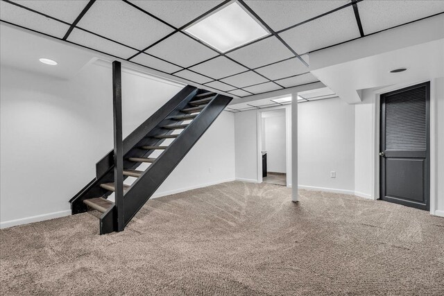 finished below grade area with carpet flooring, stairway, baseboards, and a drop ceiling
