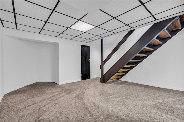 finished basement featuring carpet flooring, stairway, baseboards, and a drop ceiling