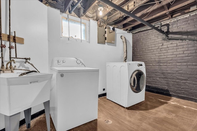 laundry area featuring independent washer and dryer, brick wall, and wood finished floors