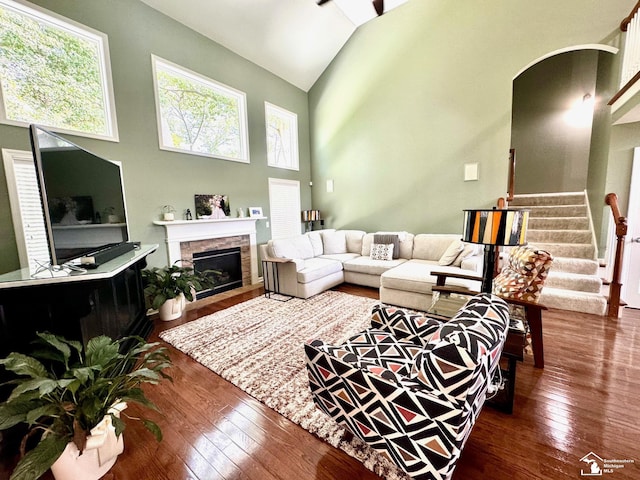 living area featuring dark wood-style floors, high vaulted ceiling, a fireplace, stairway, and arched walkways