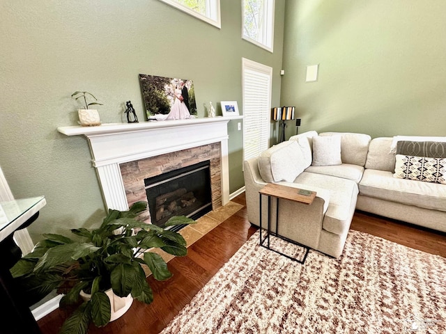 living room with a stone fireplace, wood finished floors, and a high ceiling