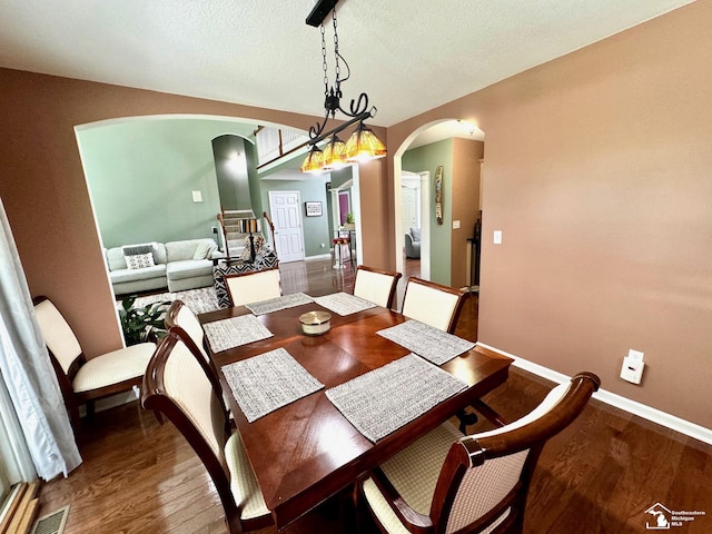 dining room with arched walkways, wood finished floors, baseboards, and a textured ceiling