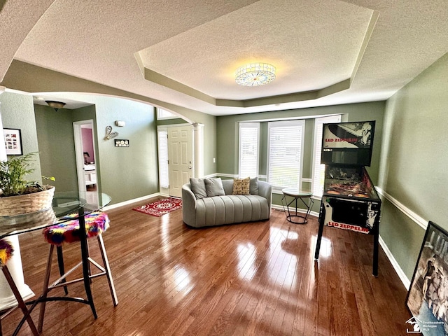 living area with a textured ceiling, arched walkways, a tray ceiling, baseboards, and wood-type flooring