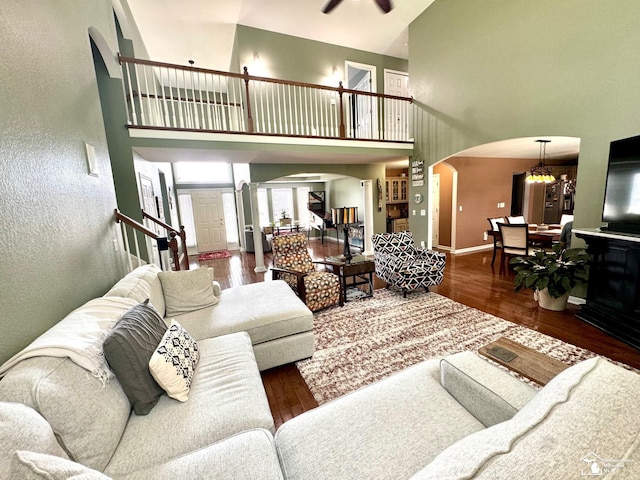living room featuring arched walkways, a high ceiling, wood finished floors, stairs, and baseboards