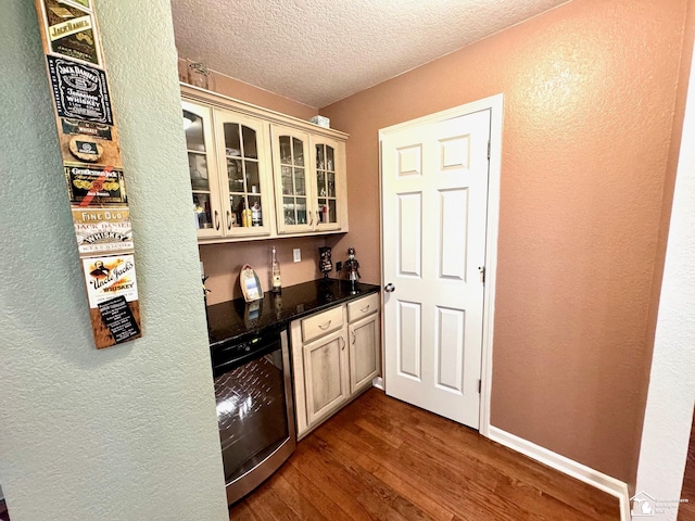 indoor dry bar with a textured wall, dark wood-type flooring, beverage cooler, a textured ceiling, and baseboards