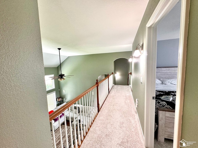 hall featuring a textured wall, lofted ceiling, and carpet