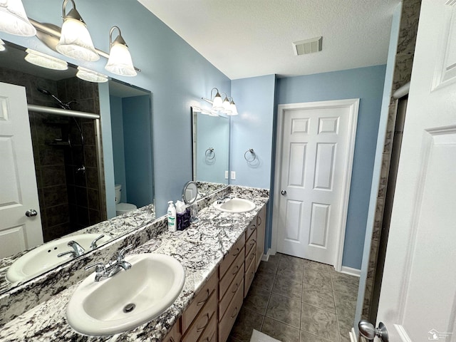 bathroom with a shower stall, toilet, double vanity, a textured ceiling, and tile patterned floors