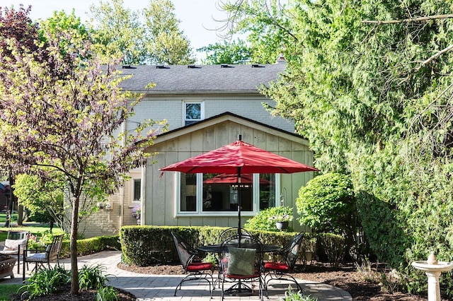 back of house featuring a patio, outdoor dining area, a shingled roof, and brick siding