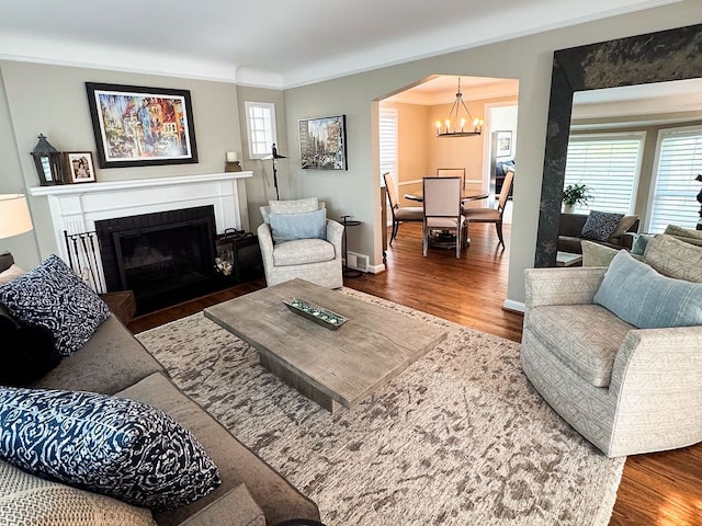 living room with a chandelier, wood finished floors, crown molding, a fireplace with flush hearth, and baseboards