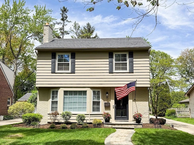 colonial house with a chimney, a front lawn, and brick siding