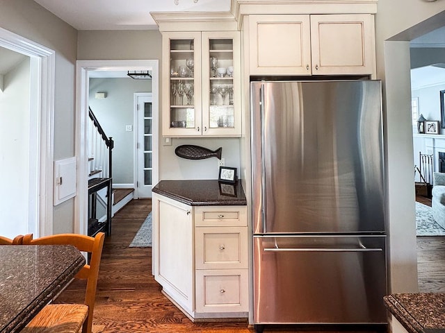 kitchen featuring freestanding refrigerator, dark wood finished floors, glass insert cabinets, and dark stone countertops
