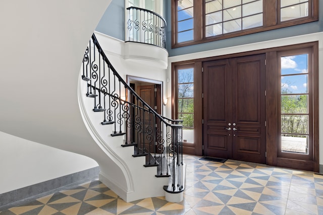 entrance foyer featuring a towering ceiling, baseboards, stairs, and light floors