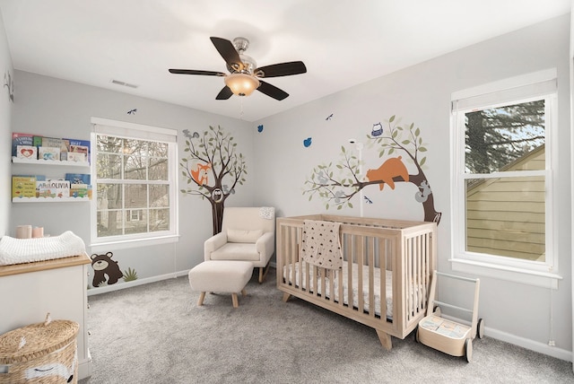 carpeted bedroom featuring a nursery area, baseboards, and ceiling fan