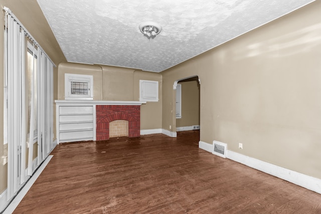 unfurnished living room featuring wood finished floors, arched walkways, baseboards, a fireplace, and a textured ceiling