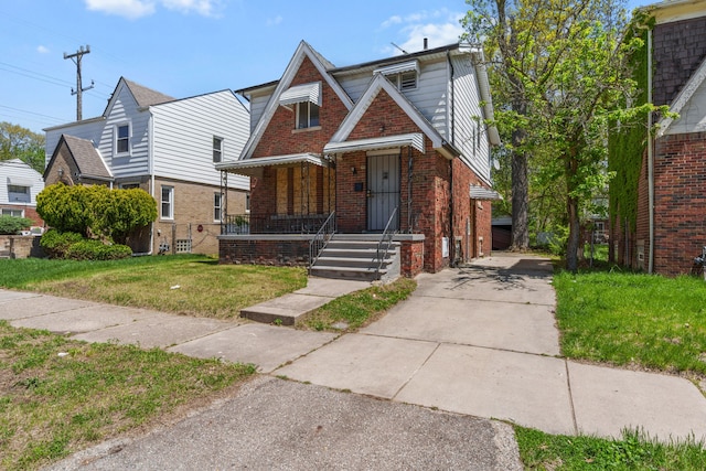 tudor-style house featuring brick siding, covered porch, concrete driveway, and a front yard