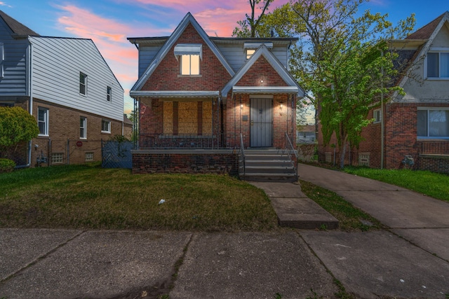 english style home featuring brick siding, a porch, and a yard