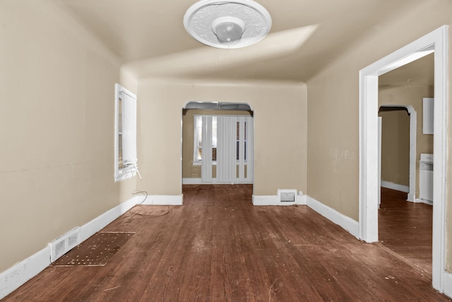 corridor featuring wood finished floors, baseboards, and arched walkways