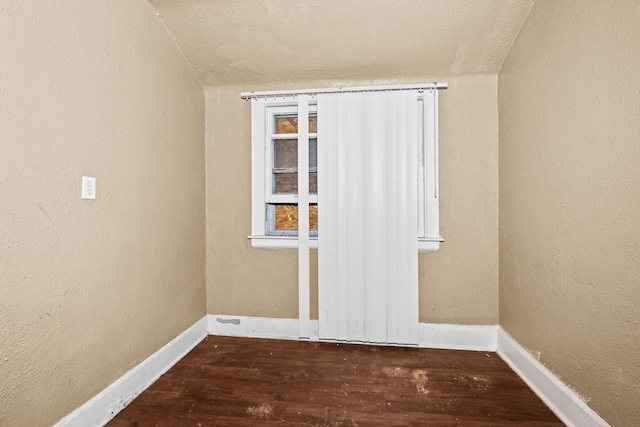 unfurnished room with wood finished floors, baseboards, a textured ceiling, and lofted ceiling
