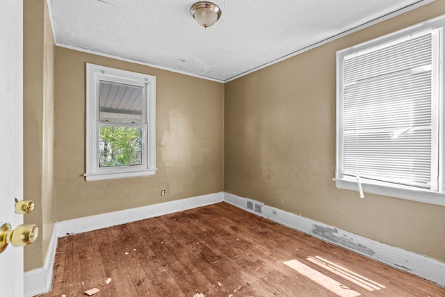 spare room featuring wood finished floors, crown molding, a textured ceiling, and baseboards