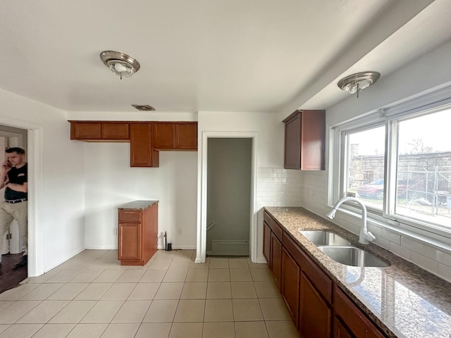 17124 Pinehurst St, Detroit, MI 48221 - kitchen featuring a sink, stone counters, backsplash, light tile patterned floors, and brown cabinets