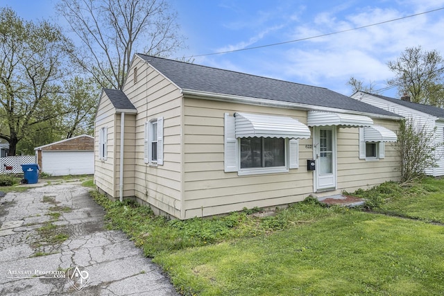 bungalow-style home with a shingled roof, a front lawn, and a detached garage