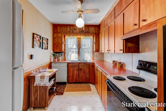 kitchen featuring white appliances, a sink, ceiling fan, brown cabinets, and wallpapered walls