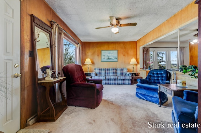 living room featuring a ceiling fan, carpet floors, wood walls, and a baseboard heating unit