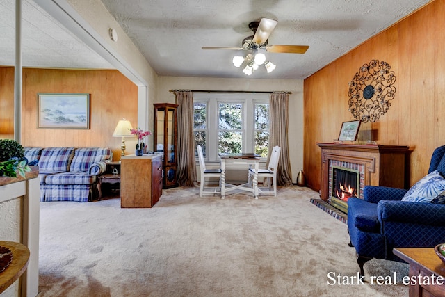 sitting room with wooden walls, carpet floors, a ceiling fan, a fireplace, and a textured ceiling