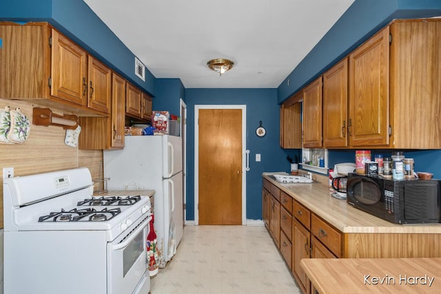kitchen with white appliances, light countertops, light flooring, a sink, and brown cabinetry