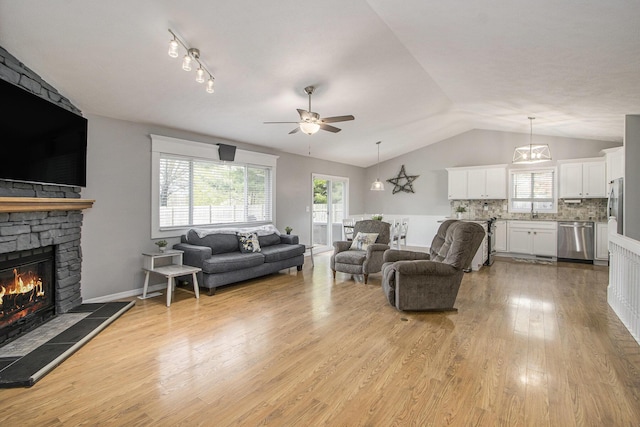 living area with vaulted ceiling, ceiling fan, a fireplace, and light wood finished floors