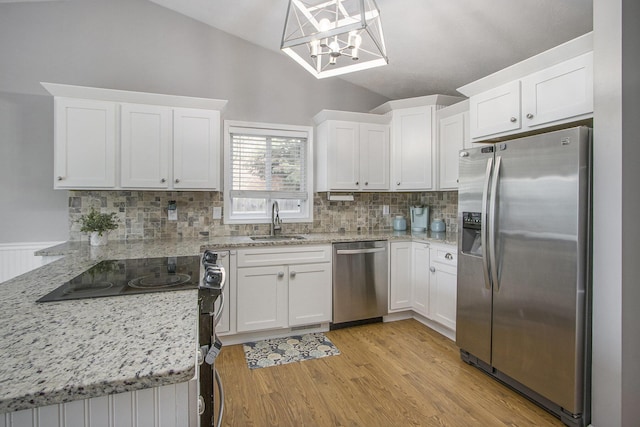 kitchen with appliances with stainless steel finishes, a sink, lofted ceiling, decorative backsplash, and white cabinetry