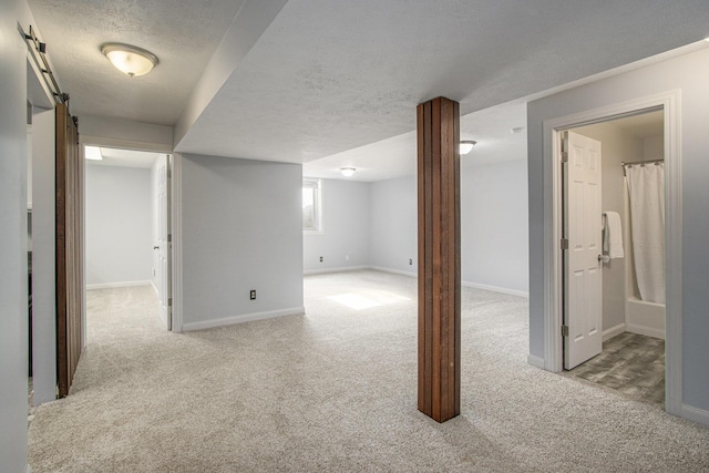 basement featuring carpet flooring, baseboards, a textured ceiling, and a barn door
