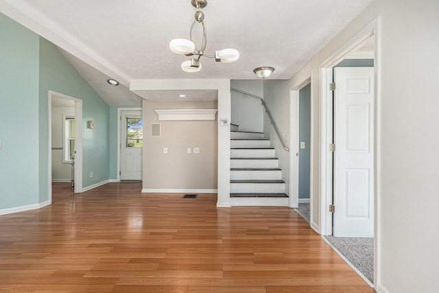 entryway with a chandelier, light wood-style floors, stairs, a textured ceiling, and vaulted ceiling