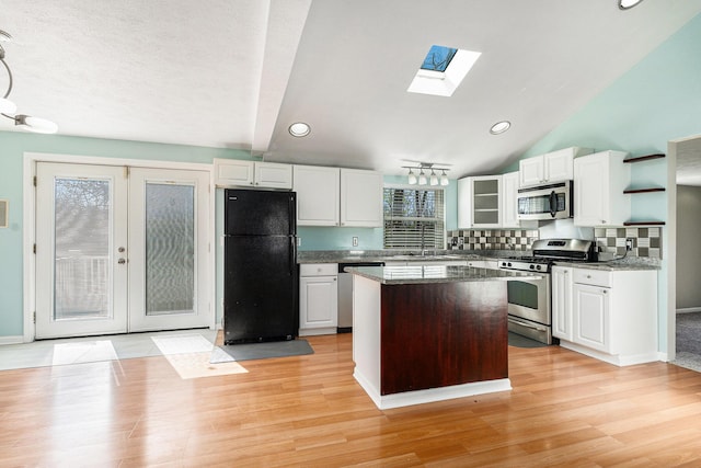 kitchen featuring appliances with stainless steel finishes, a skylight, white cabinets, a center island, and lofted ceiling